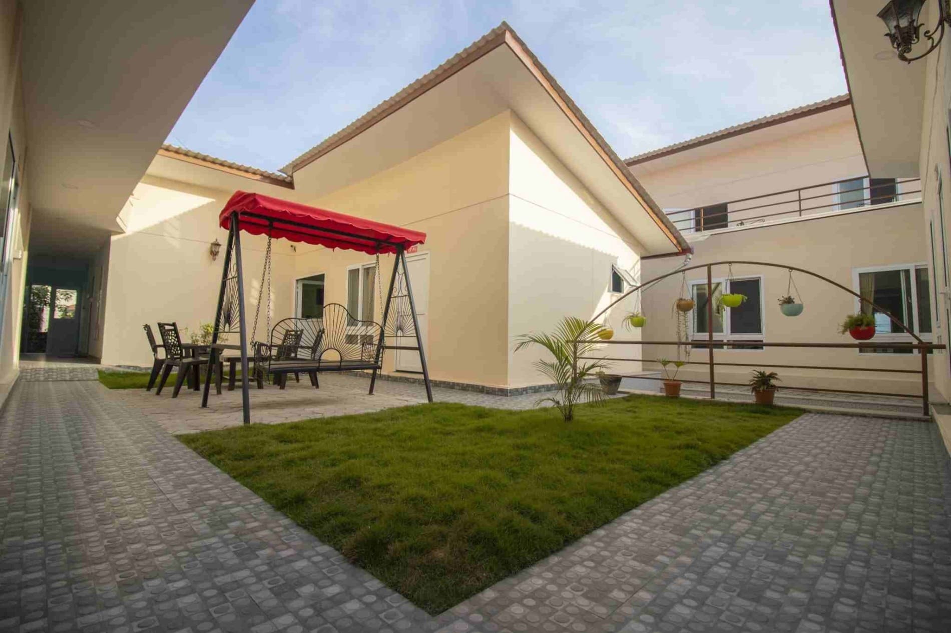 The Naman garden courtyard — red-canopy swing seat, potted plants on the railing, main building behind